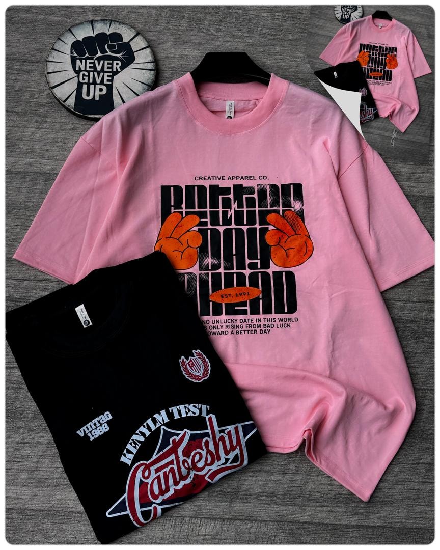Pink oversized t-shirt with Better Day Ahead peace hand graphics on hanger with folded black tee.
