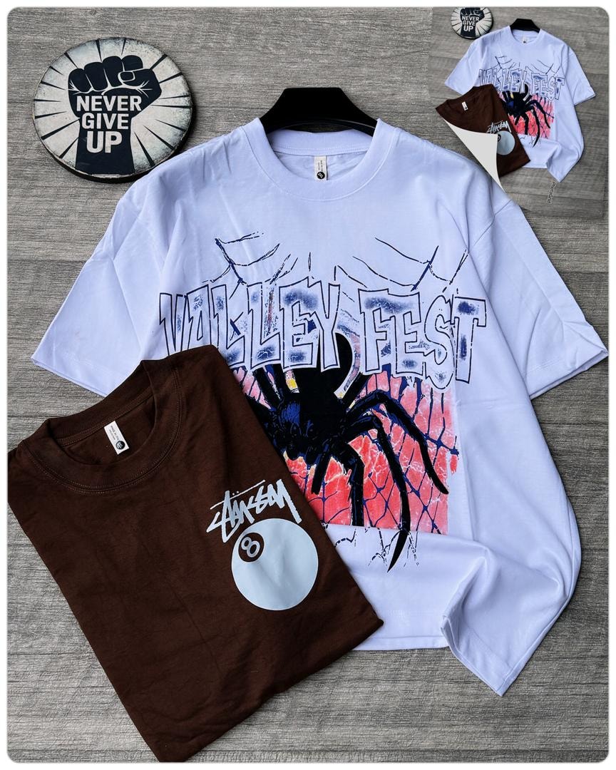 White oversized t-shirt with Valley Fest spider and web graphic on hanger next to folded brown tee.