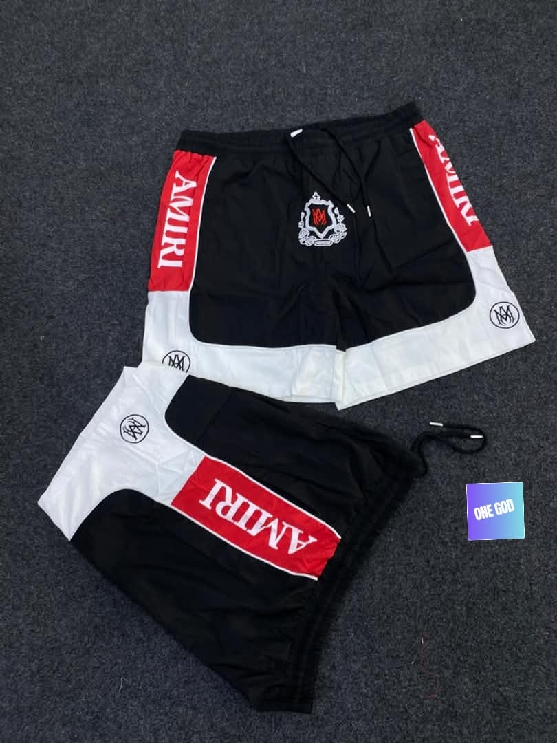 Black and white Amiri logo colorblock shorts with red band and crest.