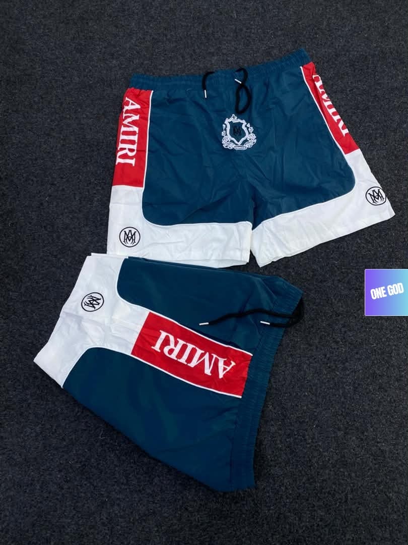 Teal and white Amiri logo colorblock shorts with red accents and crest.