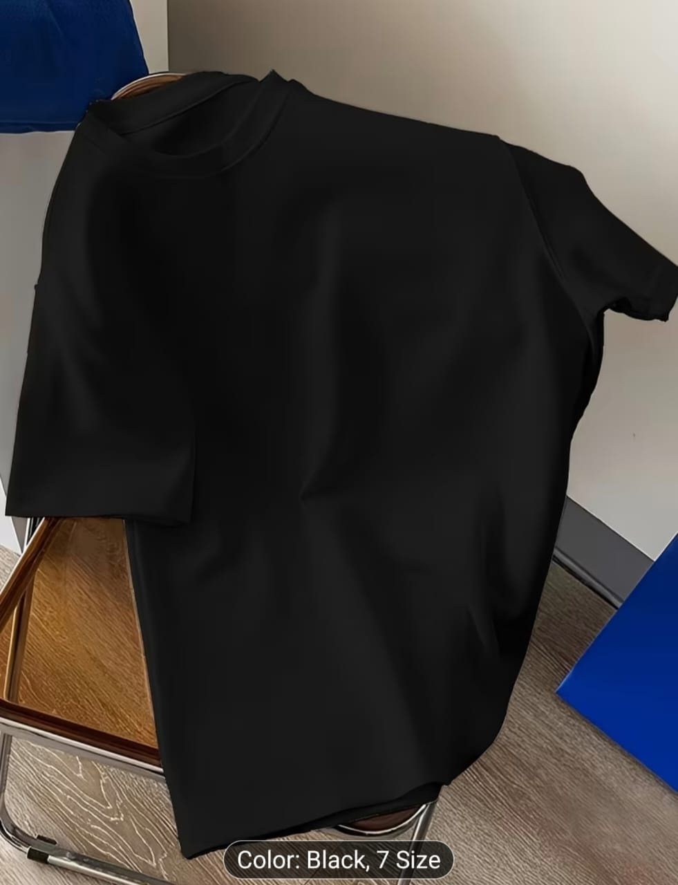 Black plain t-shirt shown from front on a wooden surface.