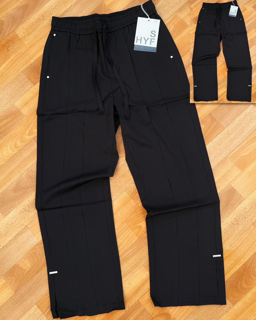 Black HYF material joggers laid flat on wooden floor with inset detail and size tag.
