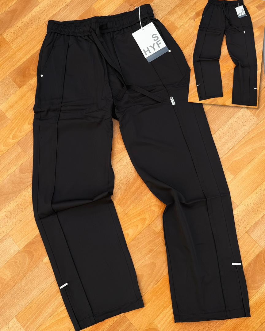 Black HYF material joggers laid flat on wooden floor with inset detail and size tag.