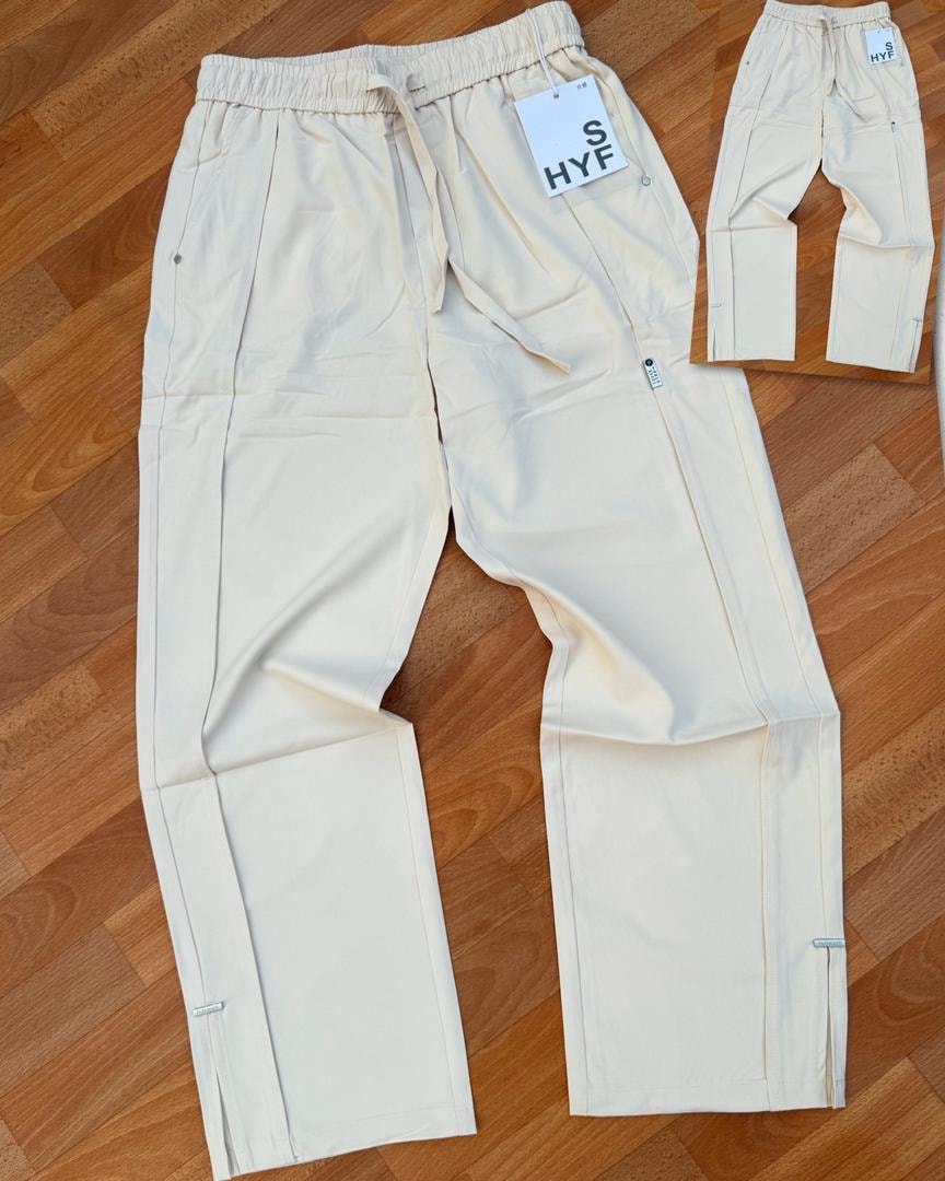 Cream HYF material joggers laid flat on wooden floor with inset detail and size tag.