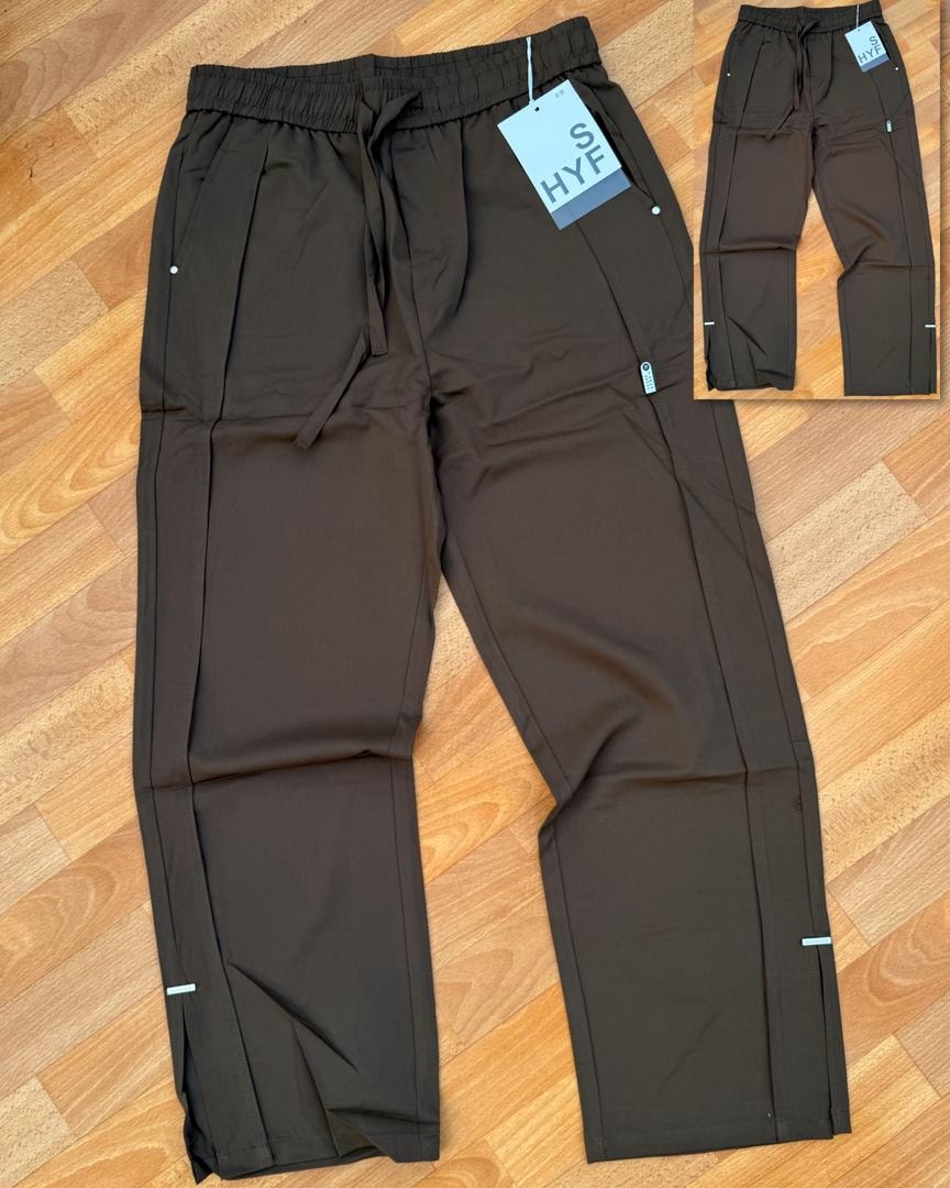 Brown HYF material joggers laid flat on wooden floor with inset detail and size tag.