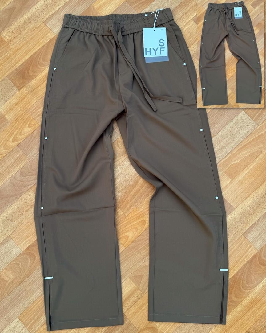Brown HYF material joggers laid flat on wooden floor with inset detail and size tag.