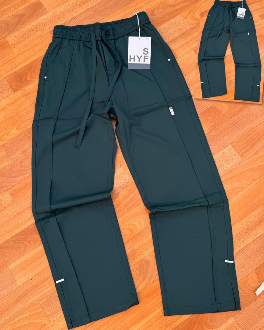 Green HYF material joggers laid flat on wooden floor with inset detail and size tag.