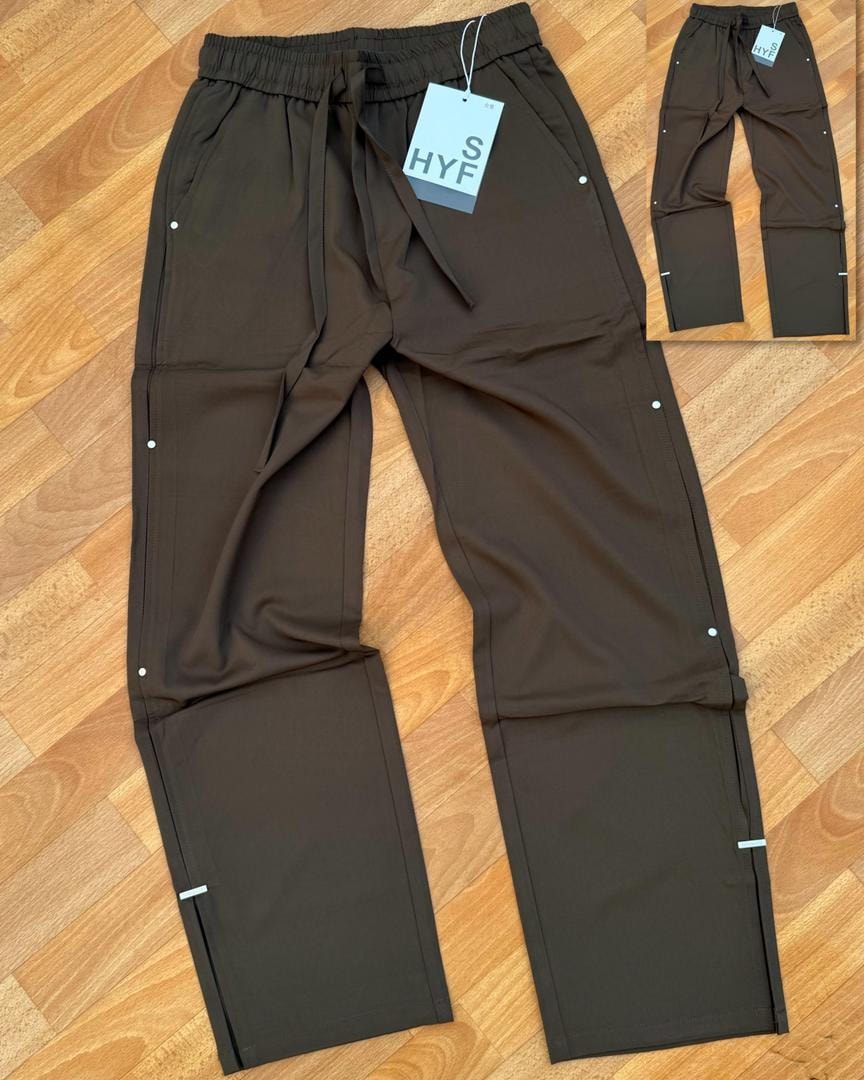 Brown HYF material joggers laid flat on wooden floor with inset detail and size tag.