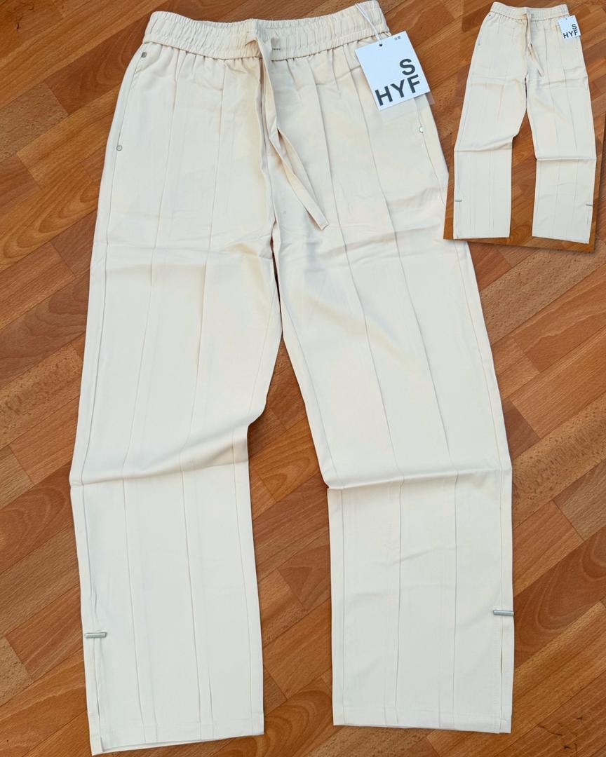 Cream HYF material joggers laid flat on wooden floor with inset detail and size tag.