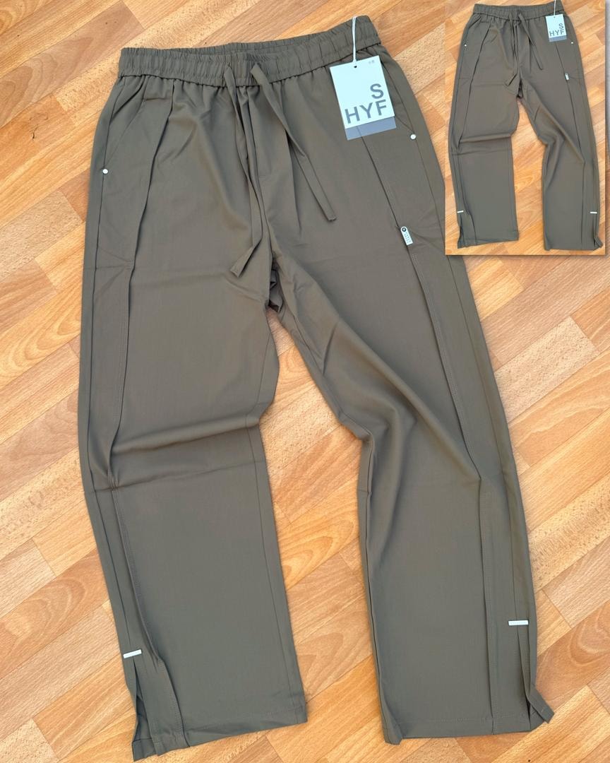 Olive HYF material joggers laid flat on wooden floor with inset detail and size tag.