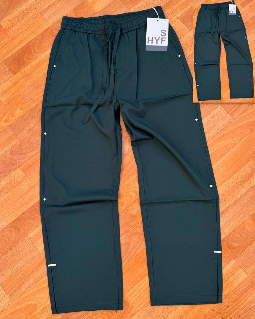 Green HYF material joggers laid flat on wooden floor with inset detail and size tag.
