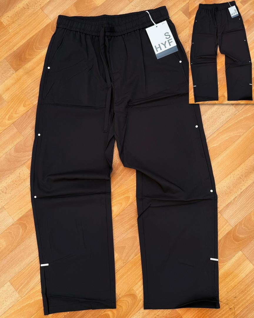 Black HYF material joggers laid flat on wooden floor with inset detail and size tag.