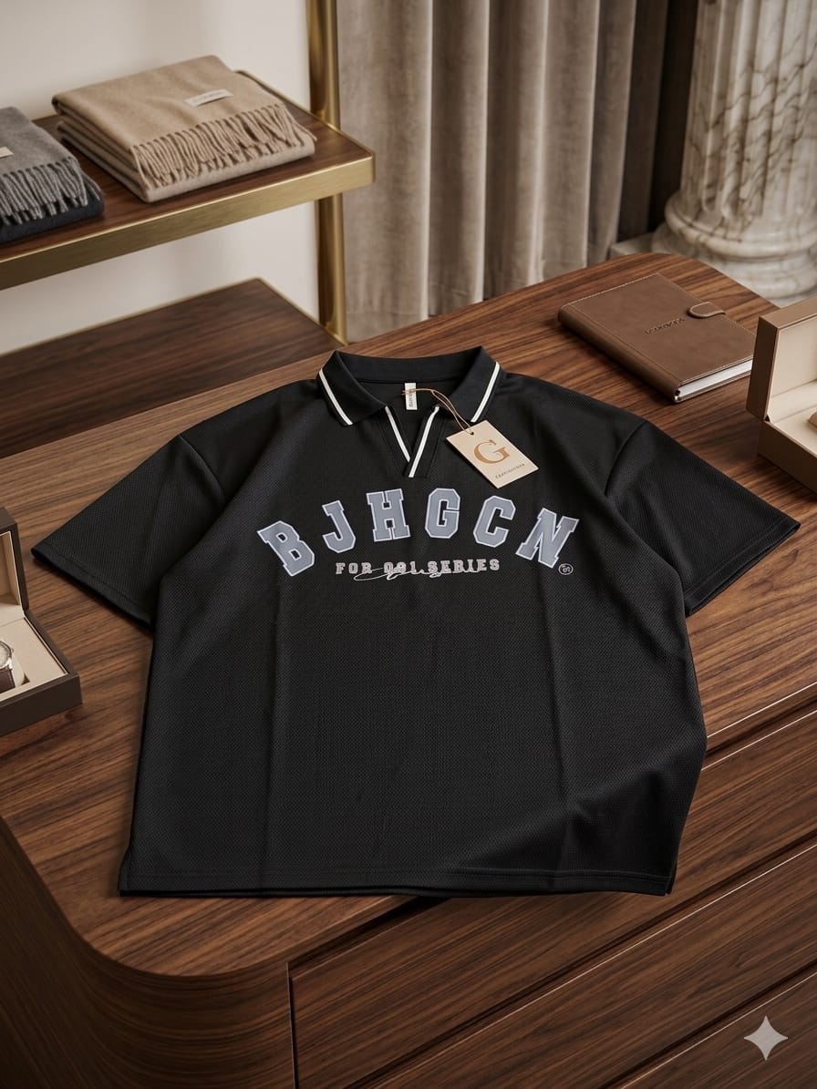 Black polo shirt with gray BJHGCN varsity print on wooden surface.
