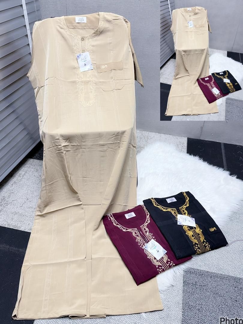 Beige embroidered jalamia with folded maroon and black ornate versions on white rug.
