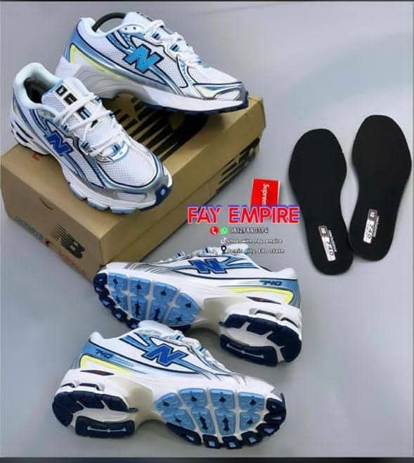 White and blue New Balance sneakers displayed with shoebox and extra black insoles.