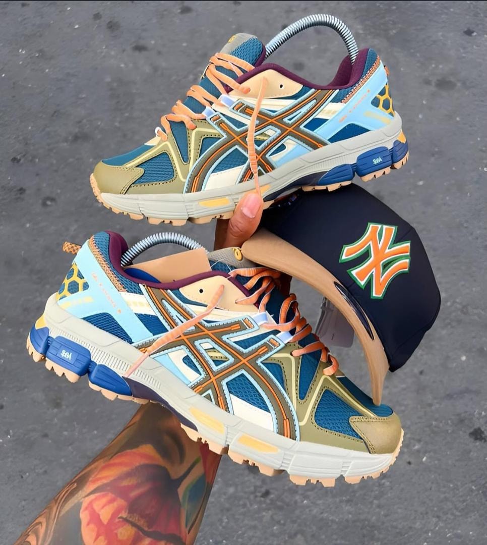 Multi-colored Asics sneakers in blue, orange, khaki and purple held with a navy cap featuring orange logo.