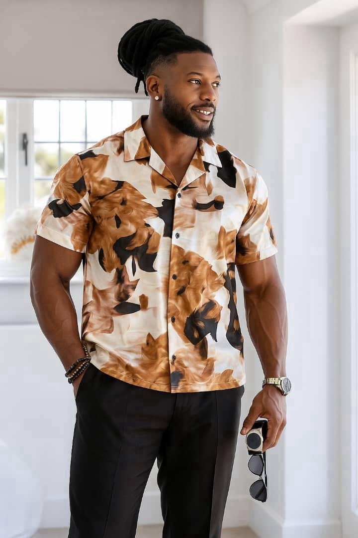 Man with dreadlocks wearing brown and black animal pattern short sleeve shirt indoors.