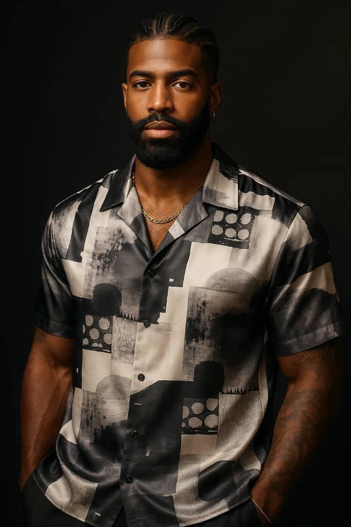 Man in black white and grey abstract geometric pattern short sleeve shirt against dark background.