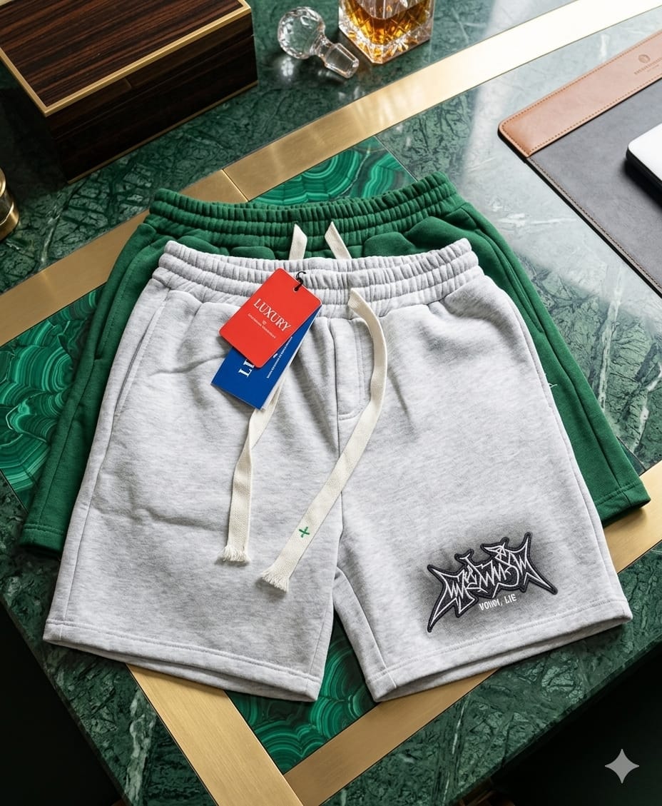 Light gray short joggers with black stylized graphic embroidery and luxury tag on green marble surface.