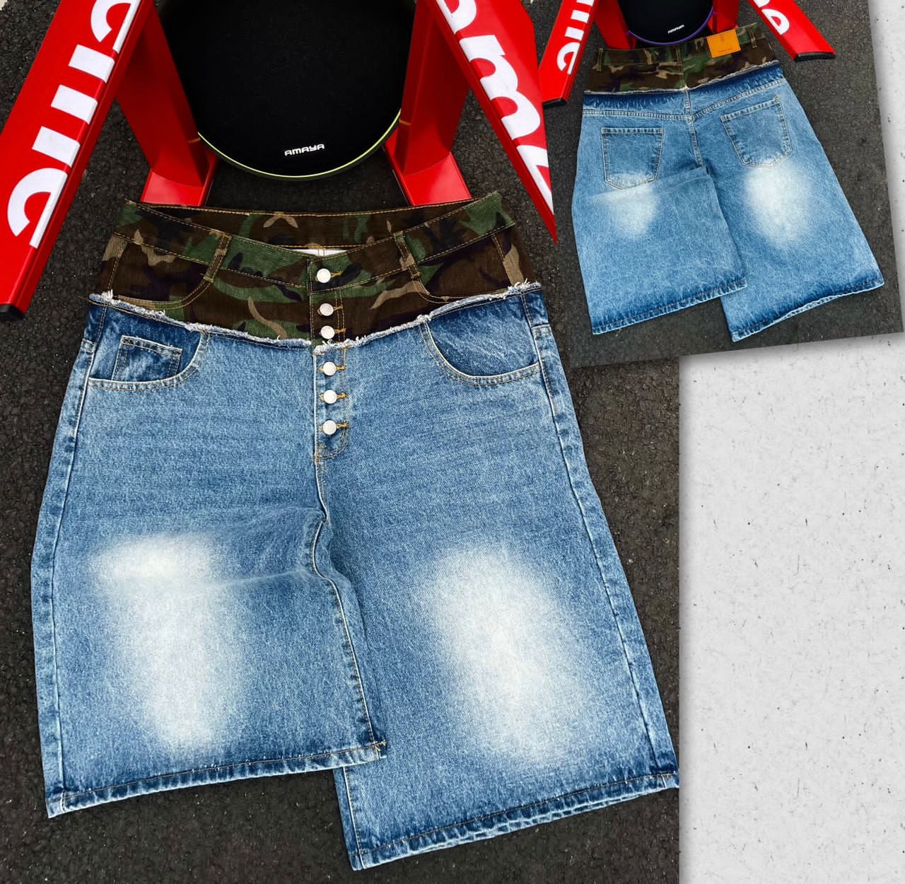Light blue 3/4 denim shorts with camouflage waistband and button fly, flat lay with accessories.