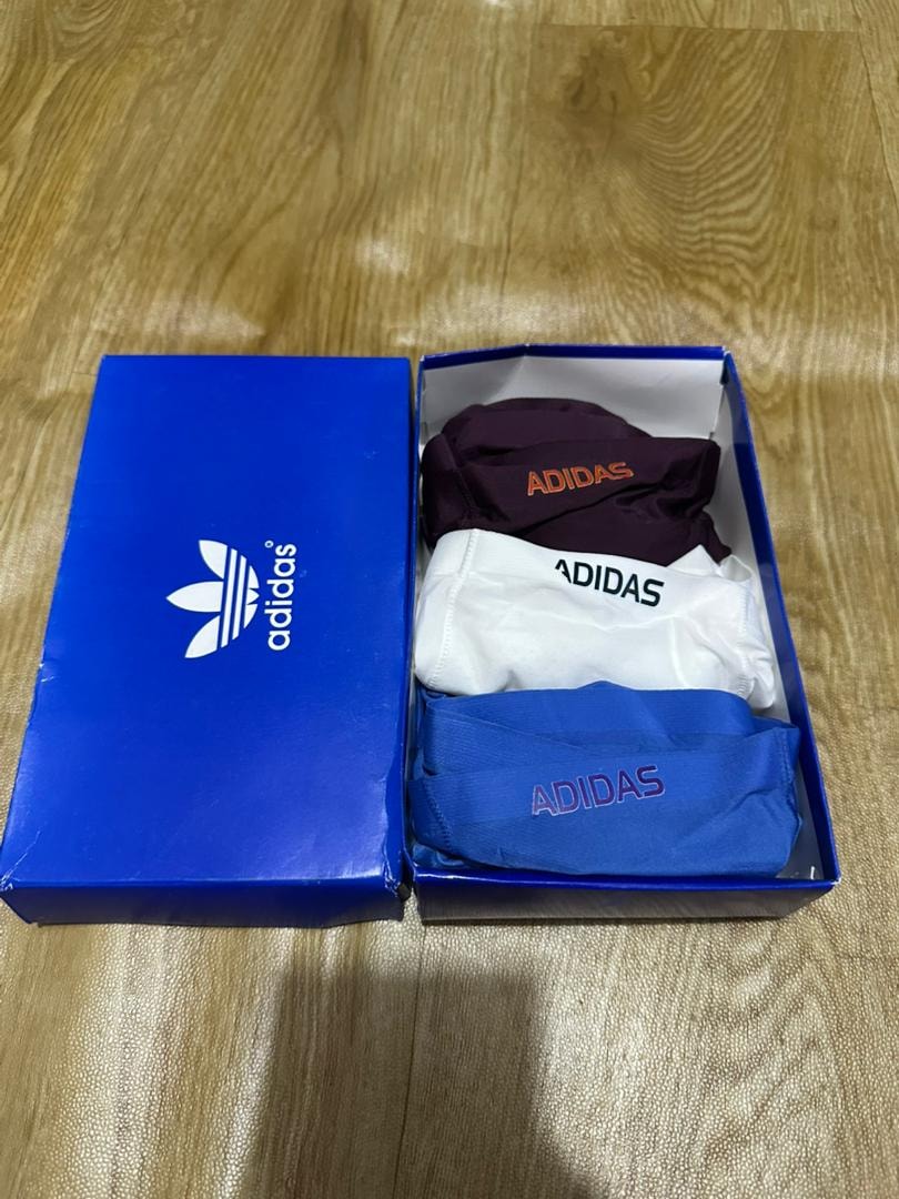 Adidas 3-pack briefs in maroon, white and blue shown in open blue box on wooden surface.