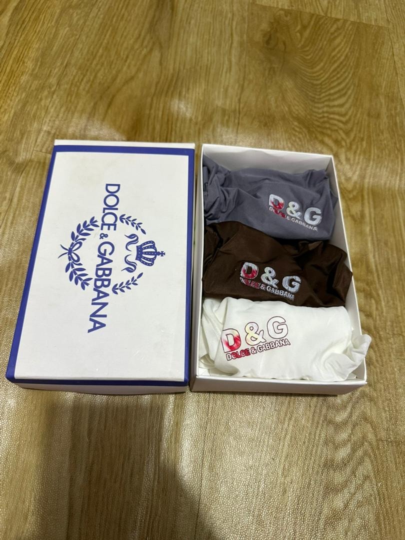 Dolce & Gabbana 3-pack briefs in grey, brown and white inside open branded box on wooden floor.
