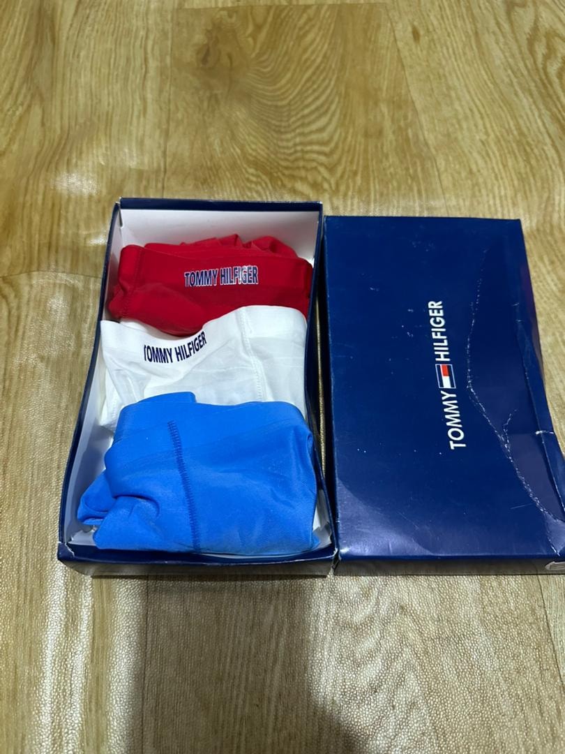 Tommy Hilfiger 3-pack briefs in red, white and blue displayed in open blue box on wooden surface.