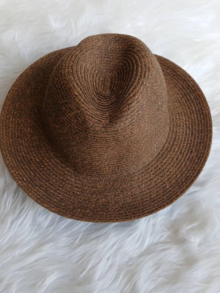 Brown woven straw fedora hat viewed from above on white surface.