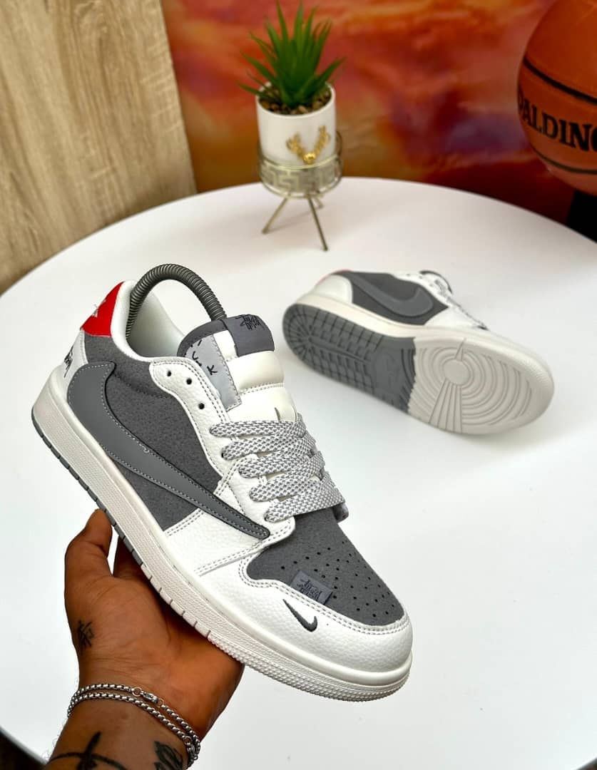Grey white and red Nike Jordan 1 Low sneakers held by hand showing side profile and sole.