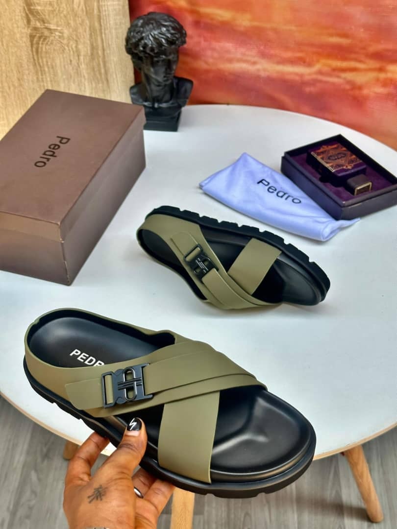 Olive green Pedro slides with buckle detail held by hand, shown with Pedro box and accessories.