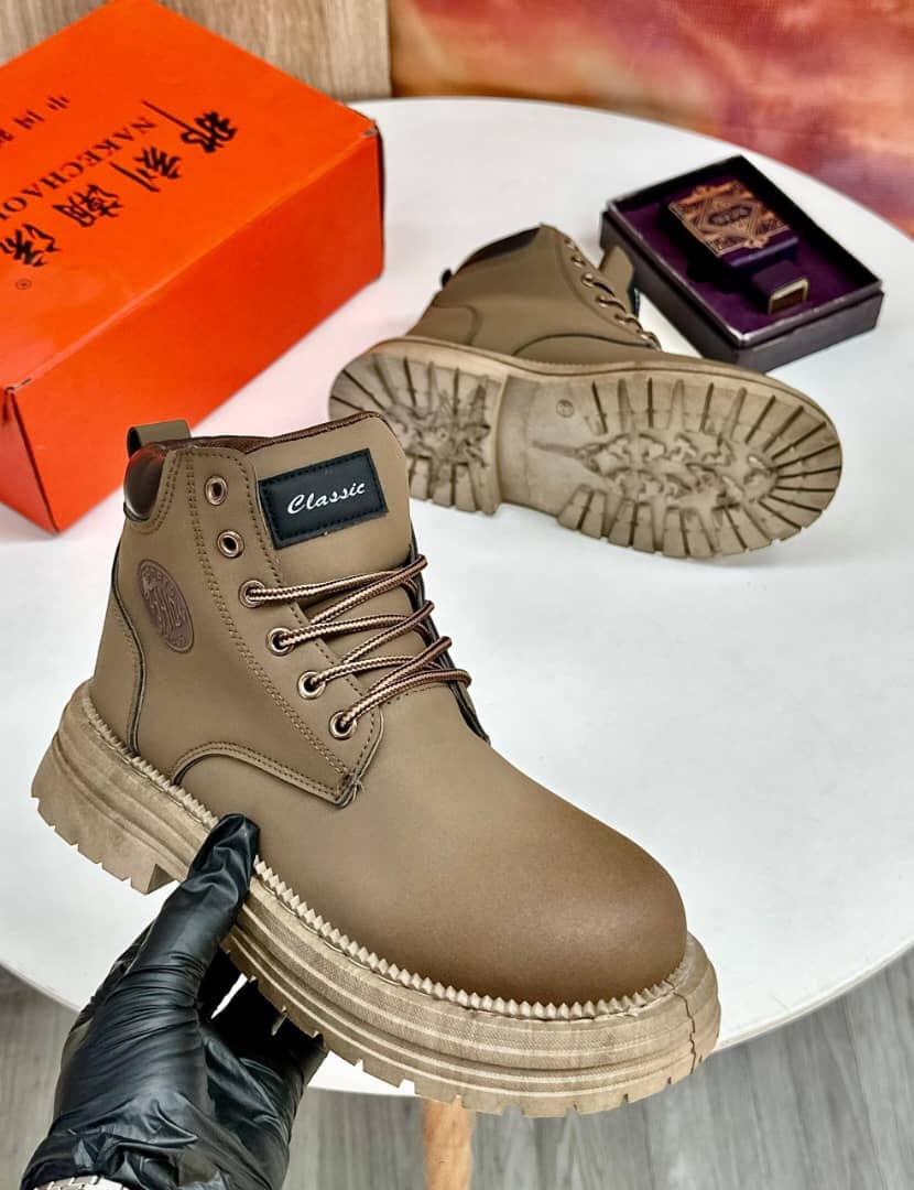 Tan combat boots held in gloved hand showing profile and sole with orange box in background.