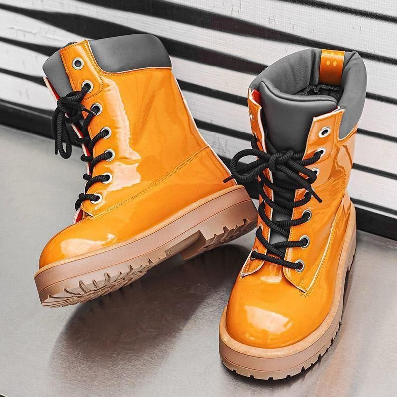Pair of glossy orange combat boots with black laces on metallic surface.