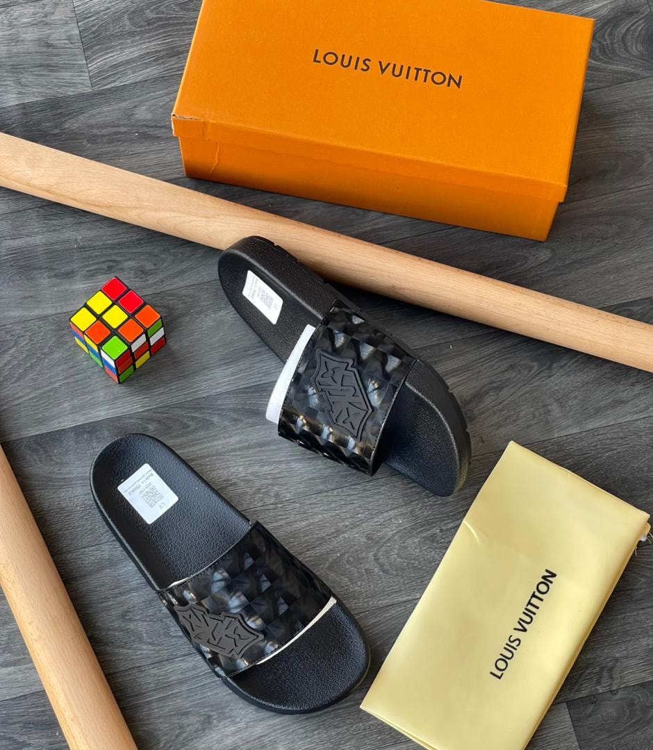 Black Louis Vuitton monogram slides with orange box and accessories on floor.
