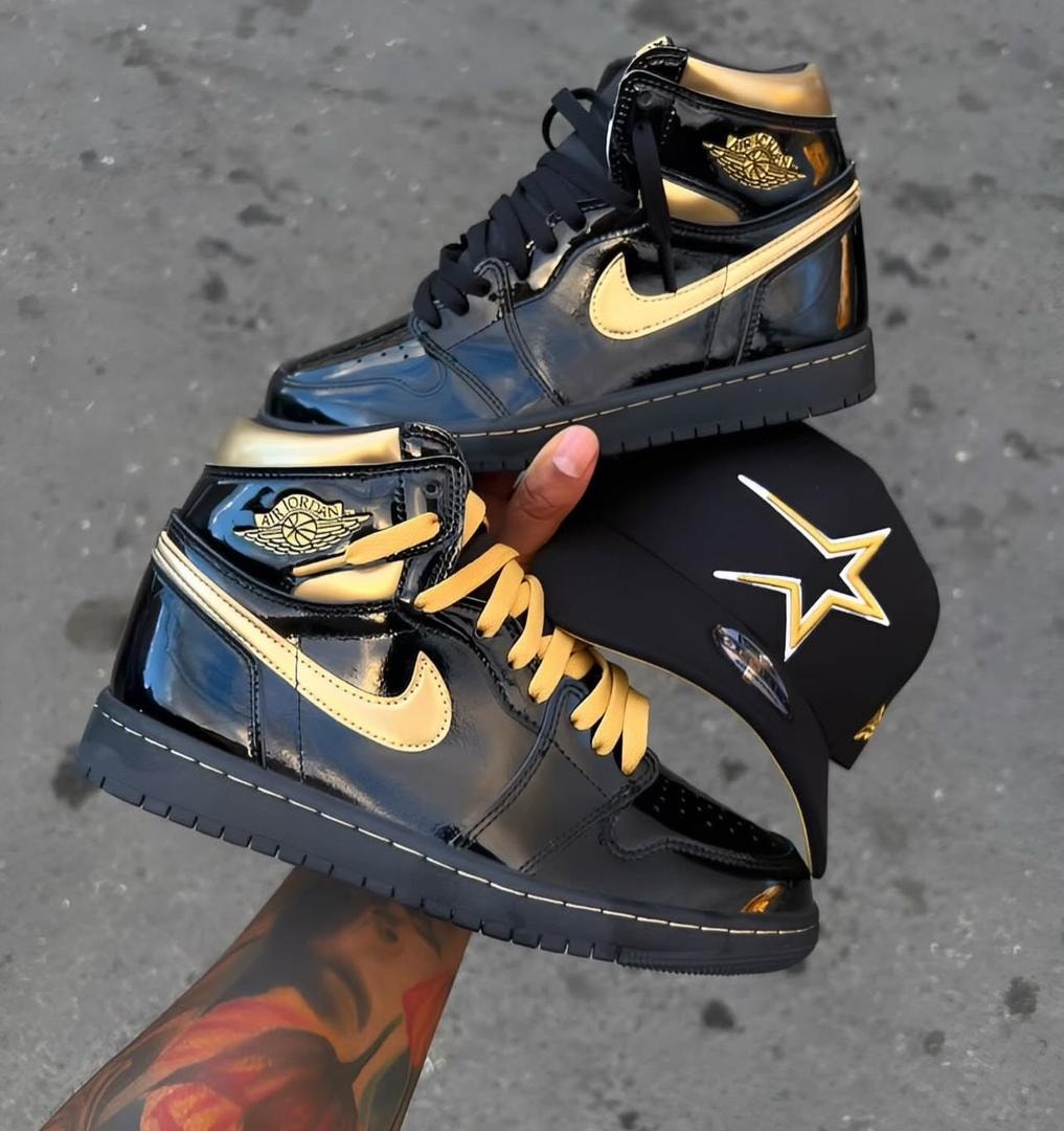 Black and gold Air Jordan 1 high top sneakers held with a branded cap.