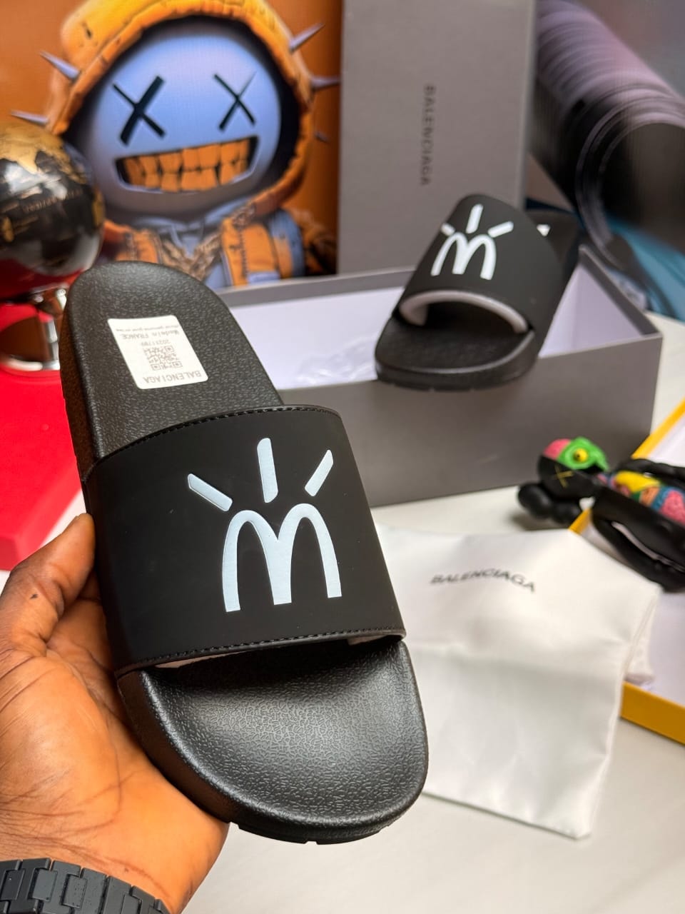 Black Balenciaga slides with white stylized logo on strap.