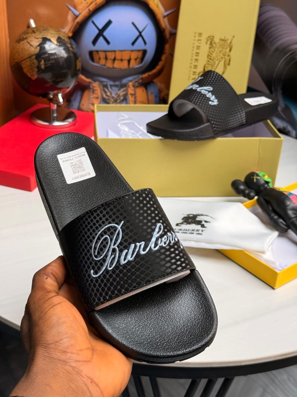 Black Burberry slides with perforated strap and cursive logo.