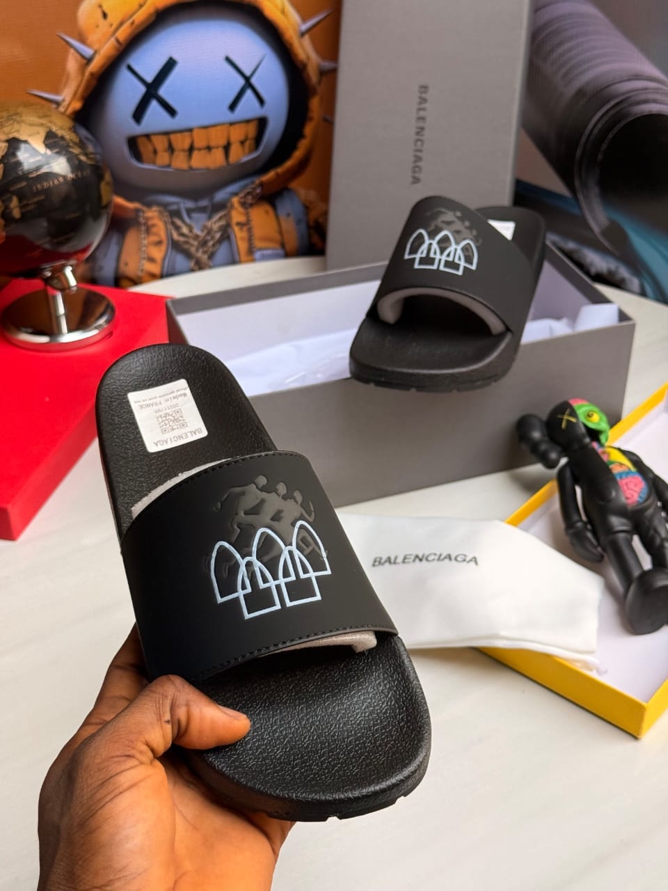 Black Balenciaga slides with white triple arch logo on strap.