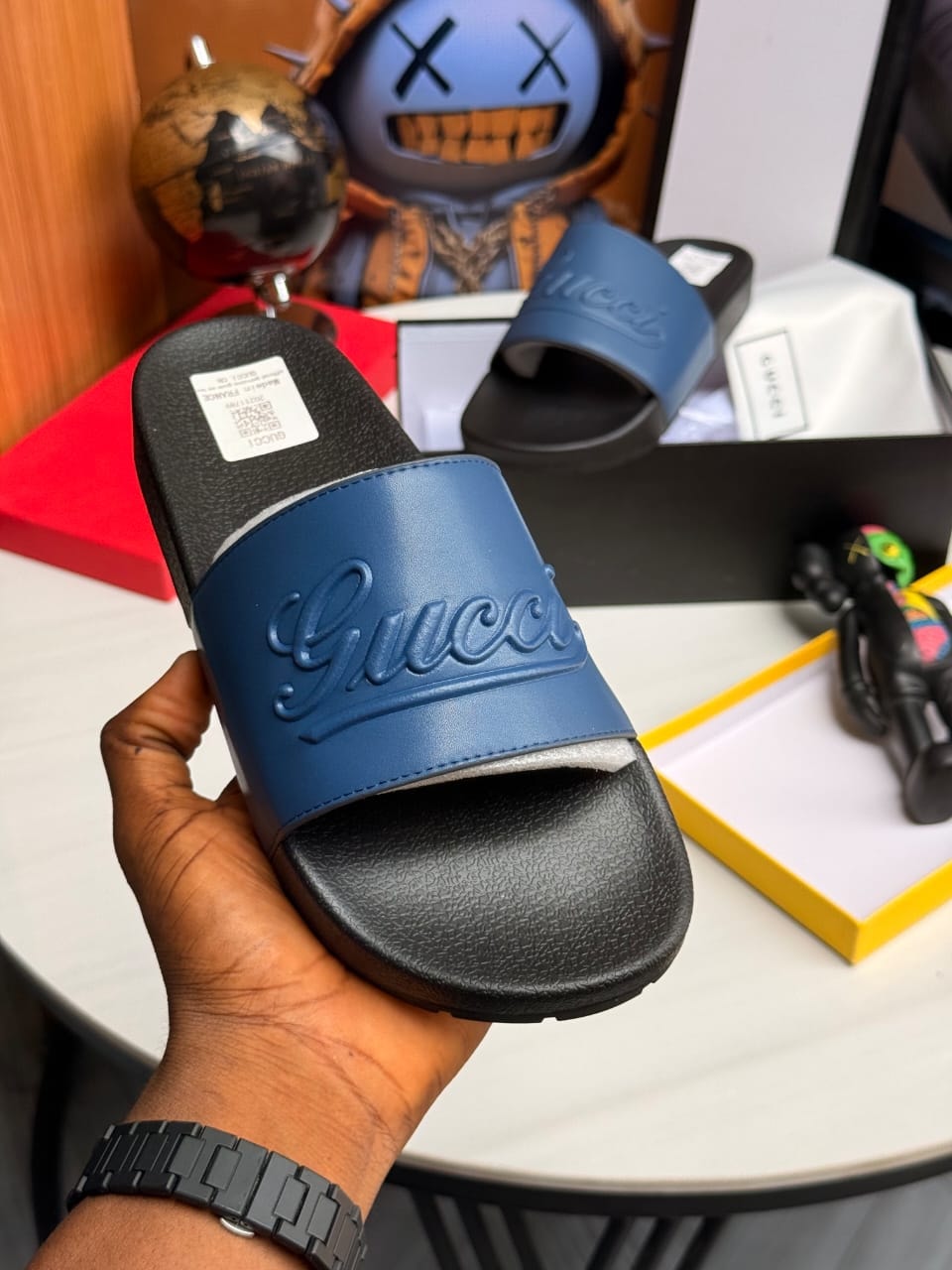 Blue Gucci slide held in hand showing embossed logo and blue strap.