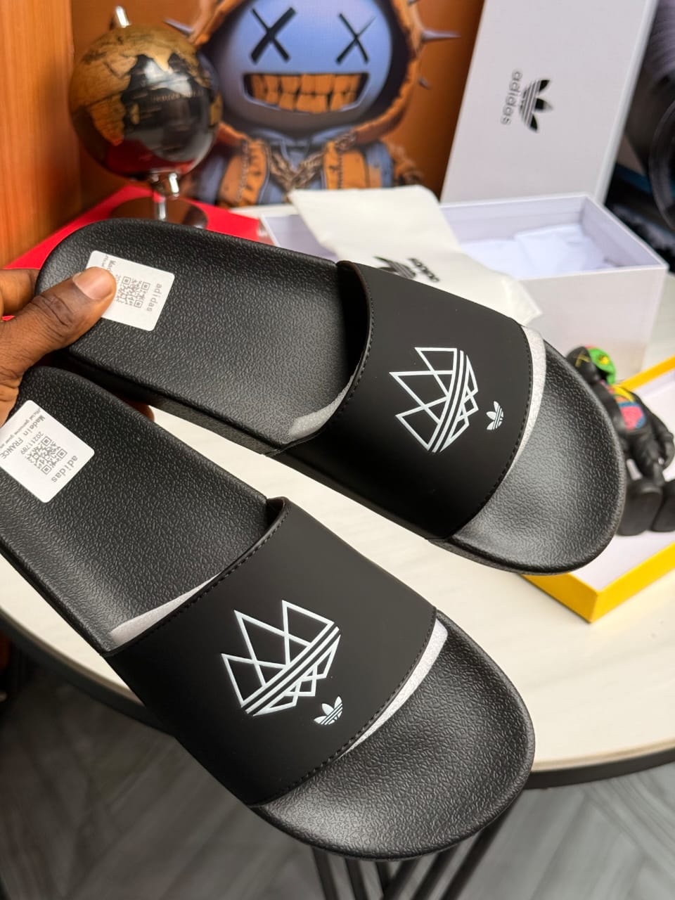 Black Adidas slides pair displayed with white logo and packaging.