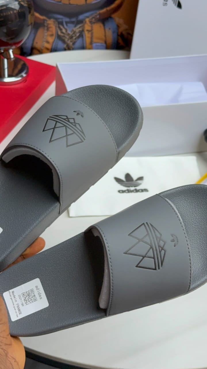 Gray Adidas slides held showing embossed logo and details.