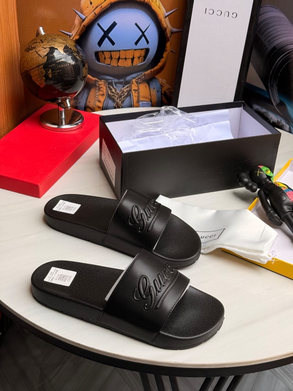 Pair of black Gucci slides displayed on table with box and dust bag.