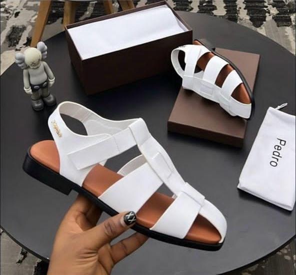 White strappy Pedro sandals held in hand with box, dust bag and figurine.