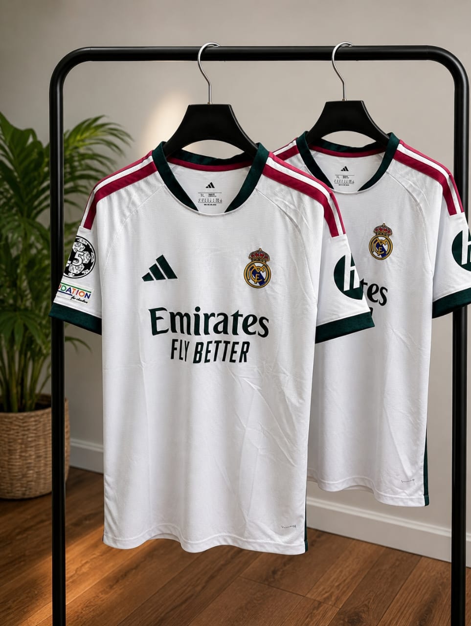 White Adidas Real Madrid home soccer jersey with green and maroon accents hanging on rack.