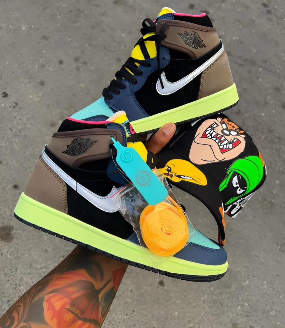 Multicolor Jordan 1 sneakers with Looney Tunes graphics held in hand.