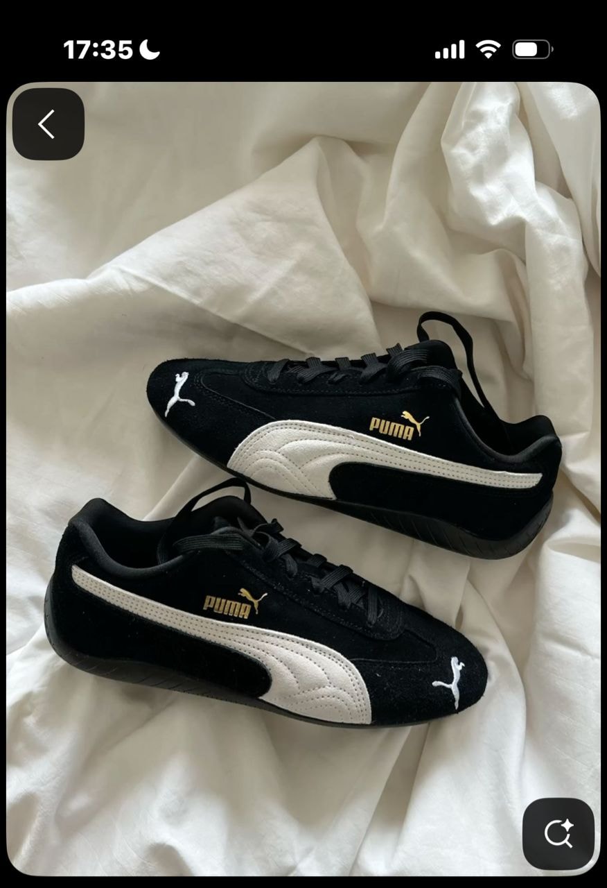 Black Puma suede sneakers with white stripe and gold branding on white fabric.