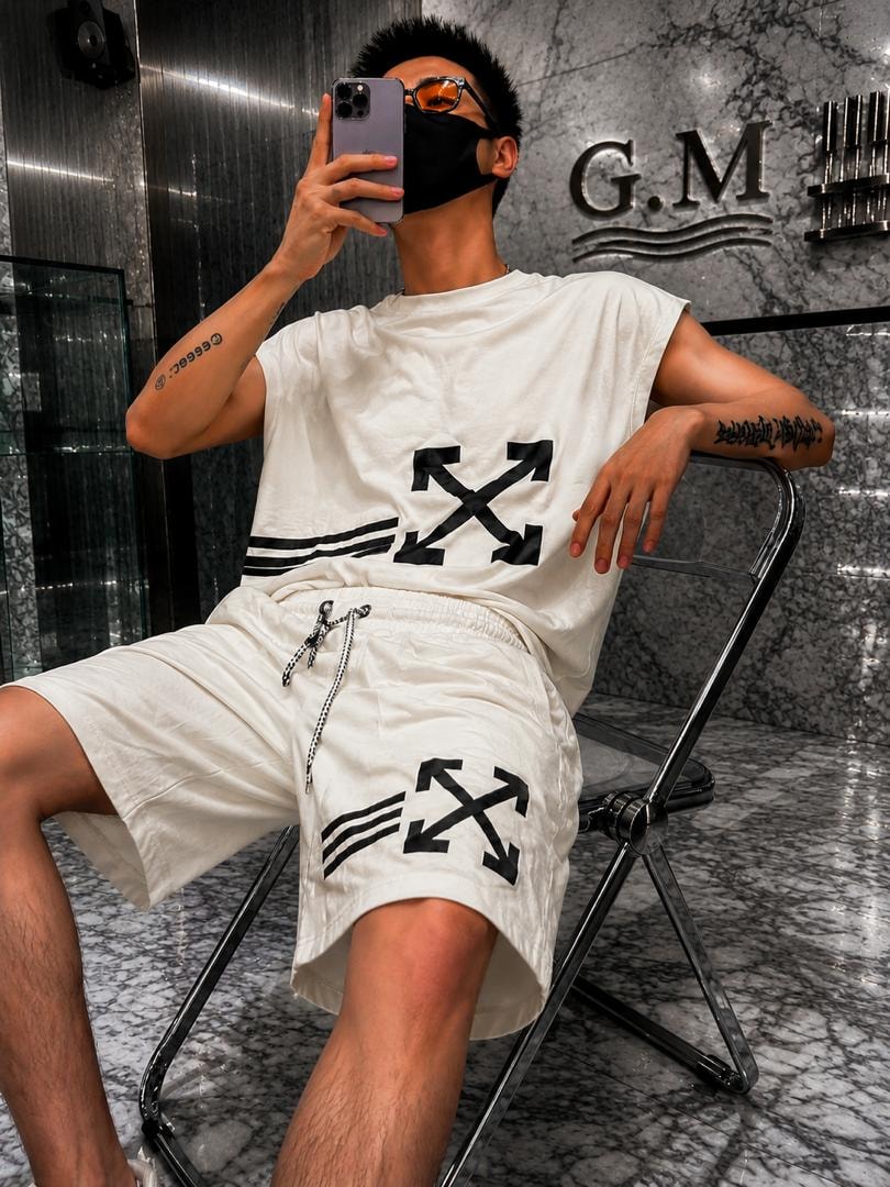 Man wearing white sleeveless top and shorts with black arrow prints, seated in modern marble interior.