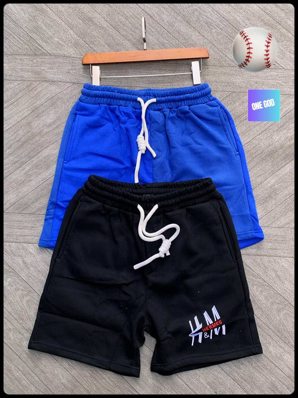 Black fleece shorts with Hermes embroidery next to blue pair on wooden hanger.