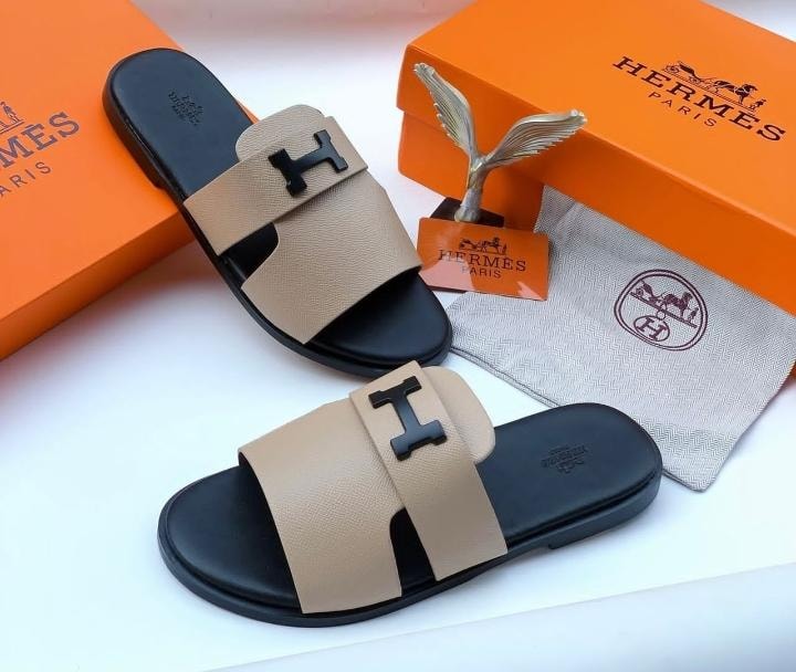 Hermes beige slide sandals with black H buckle and luxury orange packaging.