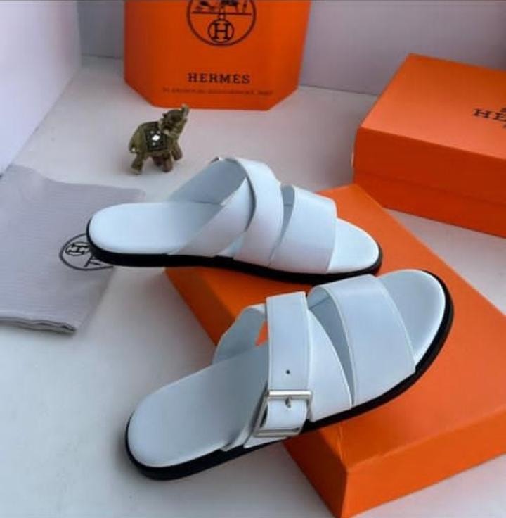 Hermes white triple strap slide sandals with buckle displayed on orange luxury boxes.