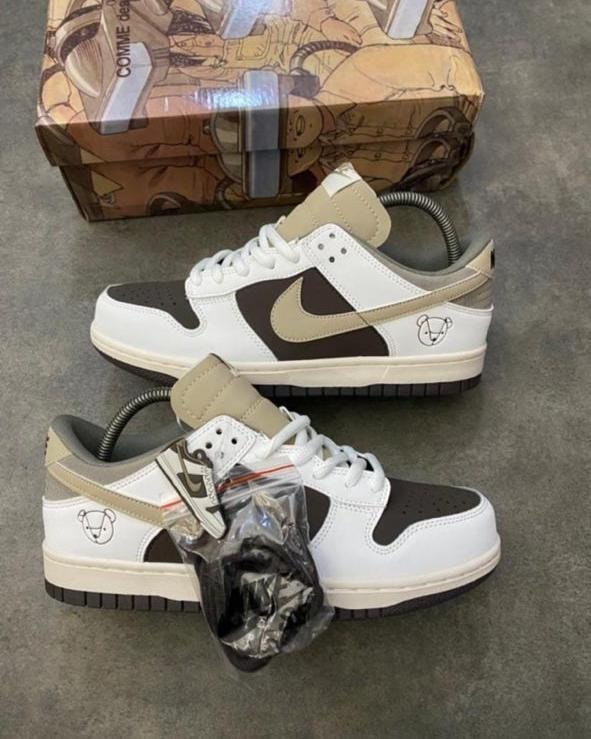 Nike Dunk Low sneakers in white brown and black with special box and accessories on gray floor.